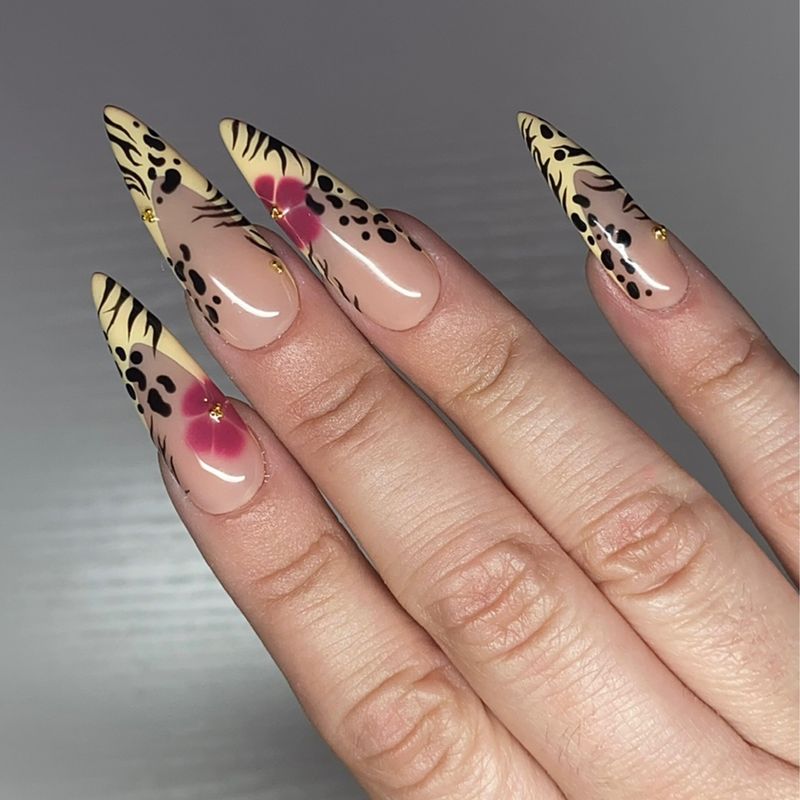 The Queen Cougar set worn on a hand — long stiletto press-on nails in tan leopard and tiger print with hand-painted magenta flowers and gold beads.